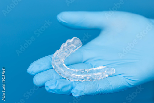 Dentist hands in gloves holding transparent dental mouth guard for night sleep, bruxism and teeth grinding prevention, orthodontic protection device on blue background, medical care and hygiene