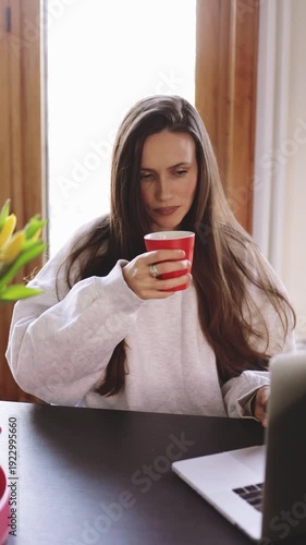 Happy young woman enjoying chocolate and coffee during work break, girl eating sweets and drinking from red cup at home office desk with laptop, cozy freelancer lifestyle