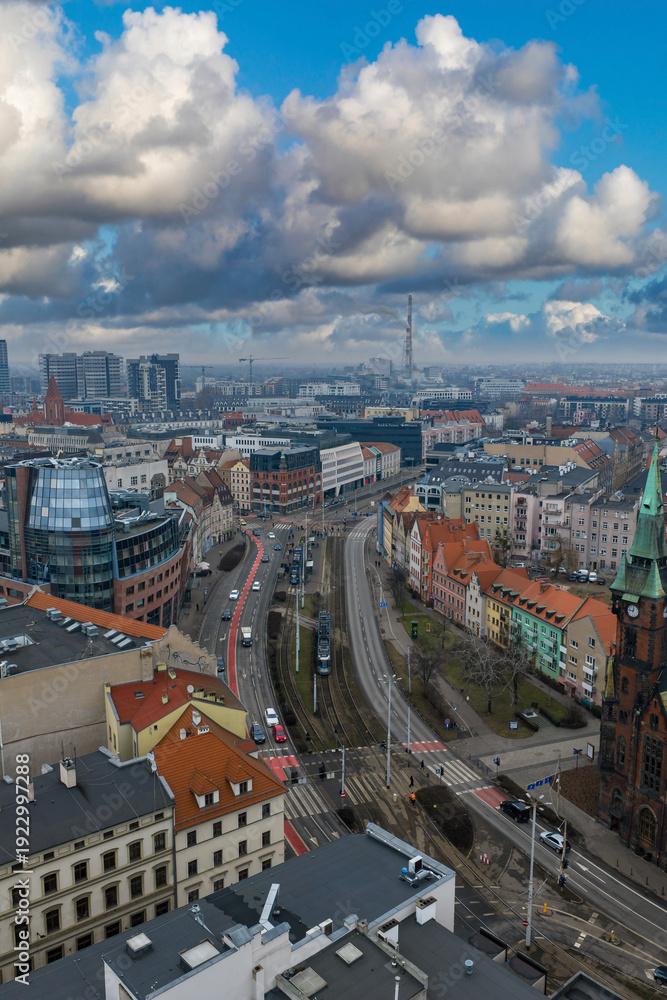 Obraz premium Daytime aerial view of Wroclaw, Poland, with red roof townhouses, modern offices, curving tram and road lines, church spire, and Wroclaw radio and TV mast after rain.