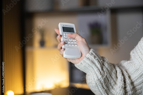 Fotografi A person holding a remote control to adjust the air conditioning while working indoors