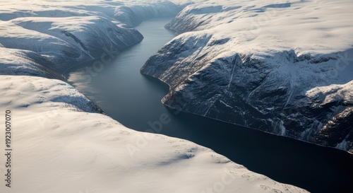 Aerial view of deep blue fjord winding between snow covered rocky mountains under soft polar sunlight, frozen winter landscape with dramatic cliffs and calm water. Concept of arctic wilderness and sol