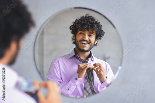 Фотография A man looks at his reflection in a round mirror while he adjusts his tie