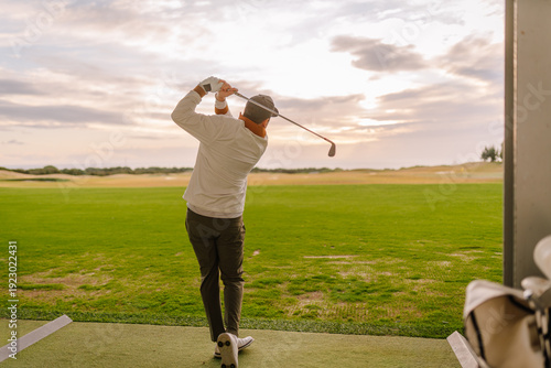 Obraz na plátně Male golfer in white long-sleeve shirt swings golf club on driving range with gr