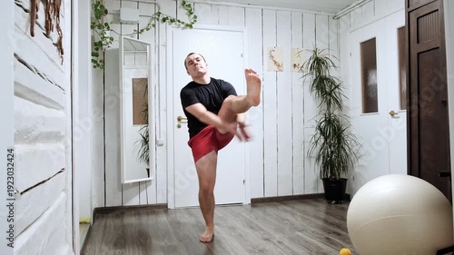 Caucasian man standing and alternately raises legs up with hand clap. Morning exercise practicing. Warm-up for the whole body at home. Healthy lifestyle. Good mood. Body care. High quality 4K footage.
