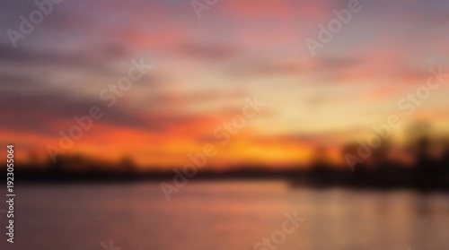 A blurred landscape showing a vibrant orange and purple sky over calm water with a dark indistinct horizon line