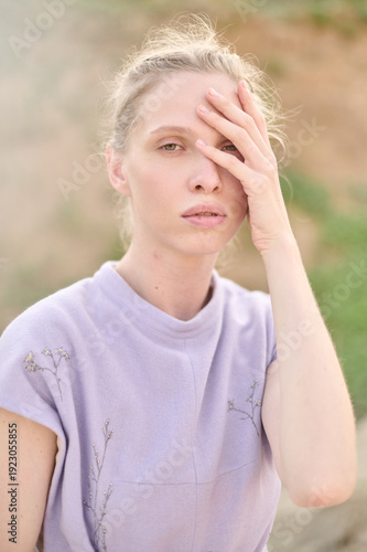 Woman in lavender dress with hand on face in soft natural light