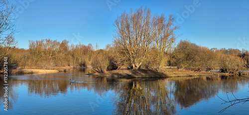 Calm lake with island and tree reflection under clear blue sky 