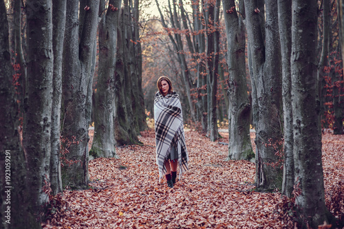 Woman walking in autumn forest wrapped in blanket