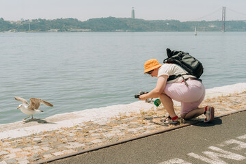 Photographer kneels near seagull on riverside promenade