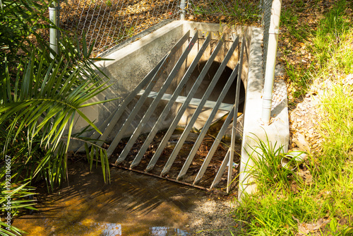 Bild auf Leinwand Concrete drainage culvert with metal grate and surrounding vegetation
