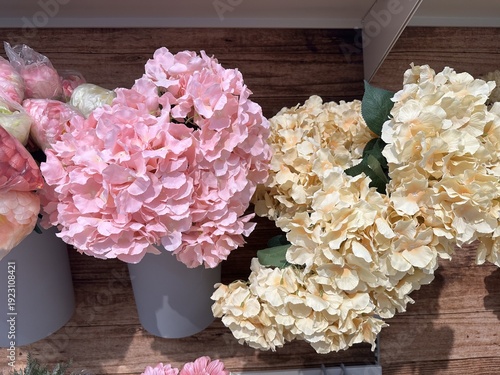Artificial pink and cream flowers displayed in white pots on a wooden surface, highlighting the intricate petal designs and vibrant colors