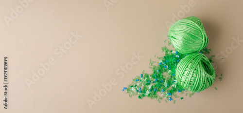 Green polyester yarn made from recycled plastic on a pile of microplastic flakes symbolizes sustainability, circular economy, and environmentally friendly production