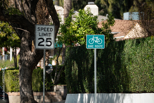 фотографія Speed limit 25 sign and bike route sign on a residential street with lush greene