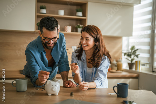 Bild auf Leinwand Happy couple saving money in piggy bank at home kitchen