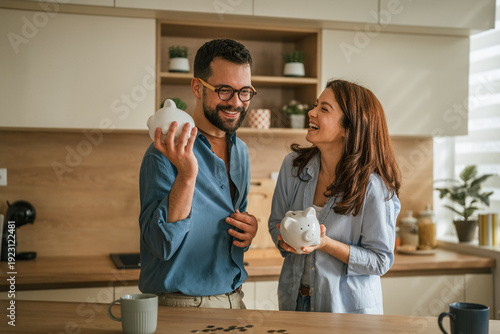 Fotografie Young couple saving money in piggy banks at home