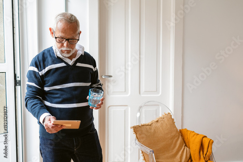 Grey-haired senior man with beard and eyeglasses standing indoors hold