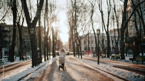 Wallpaper Mural View of a woman wearing a winter coat walking through a park at sunset, pushing a baby stroller Torontodigital.ca