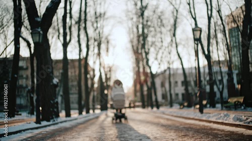 Wallpaper Mural View of a woman wearing a winter coat walking through a park at sunset, pushing a baby stroller Torontodigital.ca