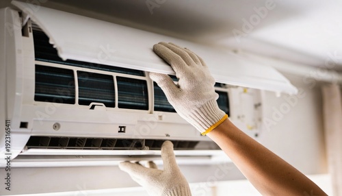 A person in white gloves is servicing a wall-mounted air conditioning unit, inspecting its internal components.