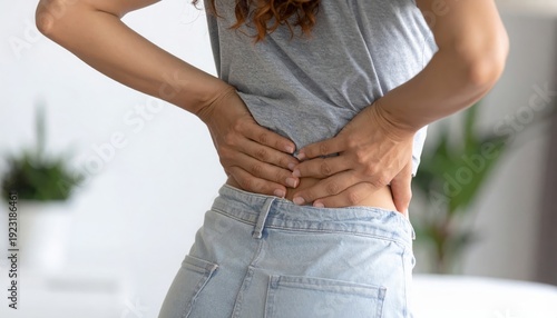 Woman suffering from lower back pain, holding her hands to her aching back, health problem.