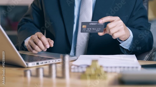 Businessman holding credit card and moving coins from high to low stack, symbolizing credit downgrade and financial risk management.