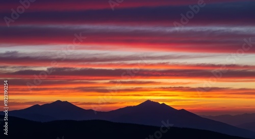 Fiery sunset illuminates mountain silhouettes with vibrant bands of color
