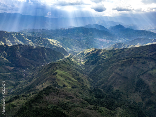 Dramatic aerial drone view of the lush green Andean mountain valleys near Vilcabamba, Loja Province, Ecuador, with spectacular god rays of sunlight breaking through dramatic clouds, illuminating the l