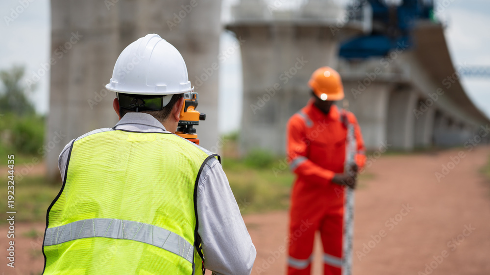 Obraz premium The survey team is operating a theodolite while referencing road construction plans. Civil engineers are taking measurements with surveying equipment at the construction site.
