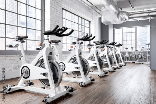 Spinning classes. A modern indoor cycling studio with rows of stationary bikes lined up against large windows, featuring a bright and clean workout environment.