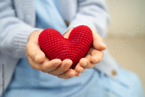 Photos Asian elder senior woman patient holding red heart in hospital.