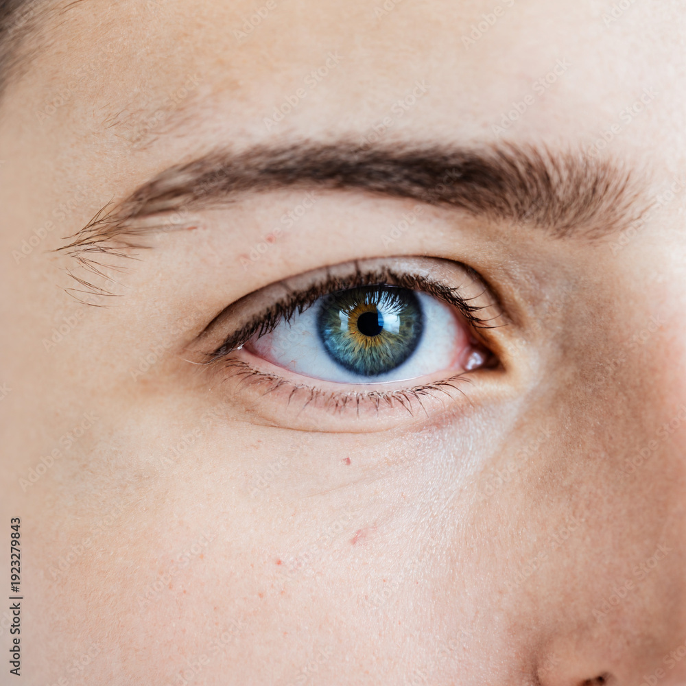 Obraz premium close up macro view of a young person eye with a blue and hazel iris showing detailed skin texture and eyelashes in natural light.