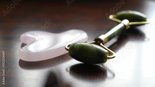 Close-up shot of a jade roller and gua sha stone sitting on a dark wooden surface, ready for skincare.