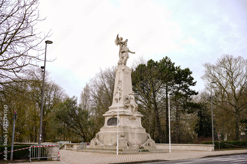Obraz premium White memorial statue on pedestal at park roundabout under cloudy sky Calais France