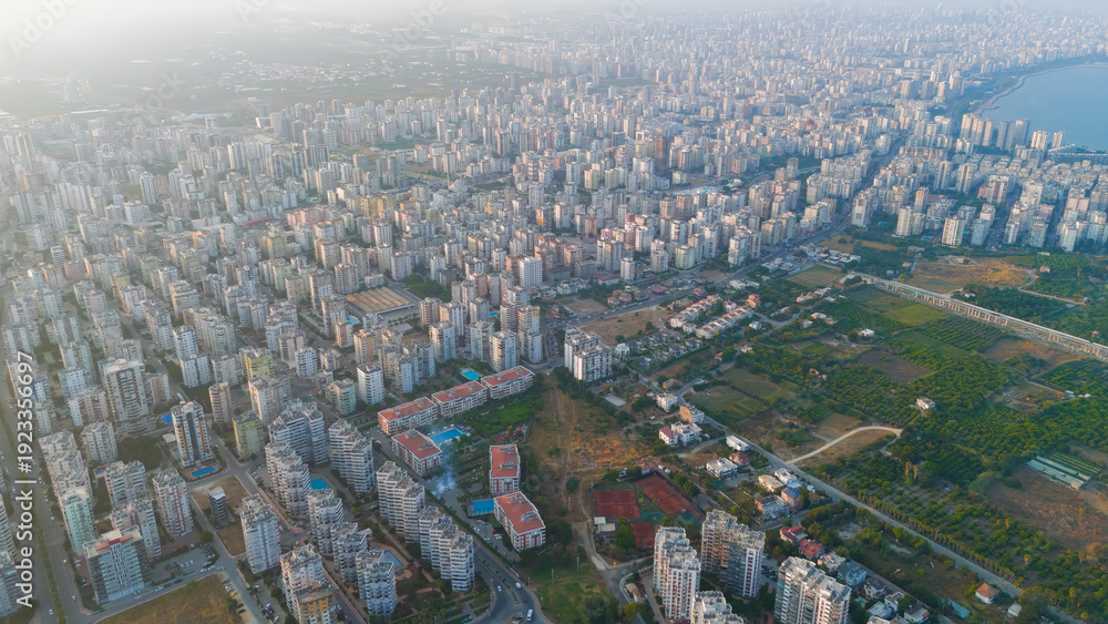 Fototapeta premium Mersin, Turkey. Aerial drone view of Mediterranean coastline at sunset. Sandy beach, sea waves, and residential district with apartment blocks in golden evening light.. Aerial View