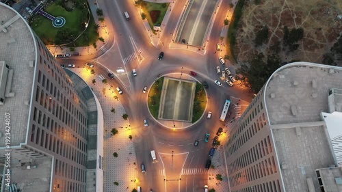 Aerial top-down drone shot of a busy urban intersection in Tangier at night. Features illuminated street lights, flowing vehicle traffic entering an underpass, and modern city architecture.