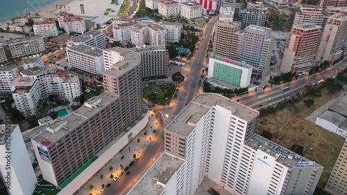 Aerial drone shot capturing the modern architecture of Tangier City Center at twilight. Features the Pestana Hotel, lit avenues, and high-rise commercial buildings in Northern Morocco.