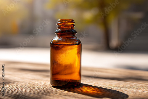 An amber glass bottle with a screw top sits on a wooden surface outdoors in natural sunlight