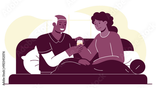 Compassionate home caregiver provides medication to a senior man while both are comfortably in bed under a blanket.