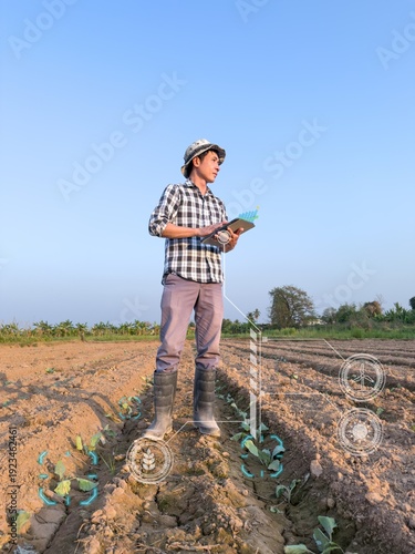 Tableau sur toile Smart Asian farmer standing in a plowed field with young seedlings, holding a digital tablet