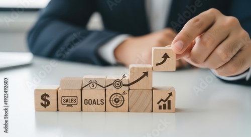 Sales forecasting model and showing cubes arranged to predict future revenue trends using wooden cubes, symbolic icons, human hand, natural depth of field, soft blurred background, clean white desk.