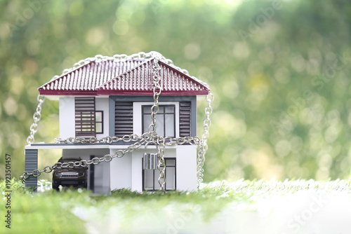 Model house locked with silver chain and padlock on green grass. Concept for home security, property seizure, foreclosure, real estate insurance, debt crisis and legal protection.