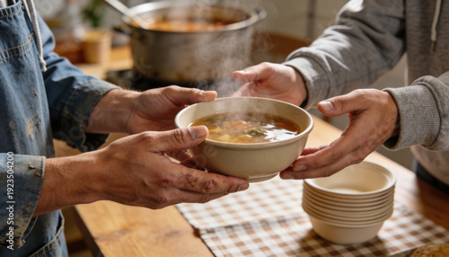 A close-up of hands respectfully passing a warm bowl of soup to a person at a community soup kitchen