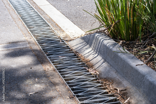 Photos Urban street curb with stormwater drainage grate and roadside gutter system beside a paved roadway