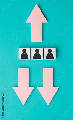 Pink arrows pointing up and down with wooden blocks featuring black human figures on a turquoise background, illustrating concepts of growth and decline in a visual format