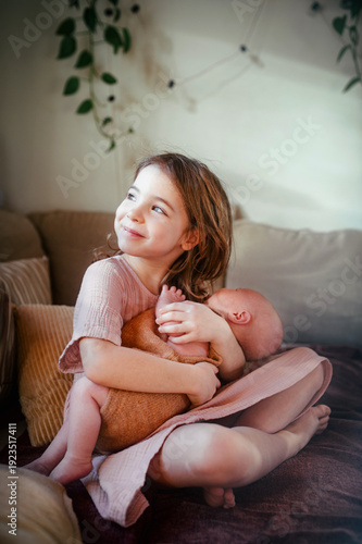 Fotografía Young girl holding newborn sister. Tender sibling moment.