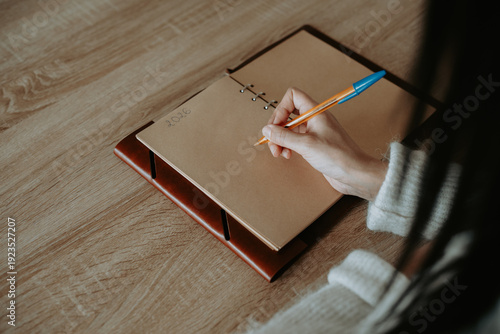 Une femme écrivant à la main dans un carnet artisanal sur une table en bois