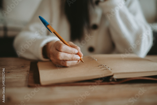 Une femme écrivant à la main dans un carnet artisanal sur une table en bois