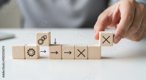 Process improvement initiative and showing cubes arranged to eliminate a known inefficiency using wooden cubes, symbolic icons, human hand, natural depth of field, soft blurred background, minimal des