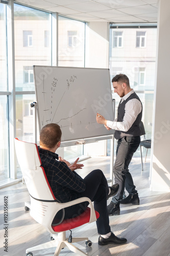 Two Caucasian men discussing work at a white board. 