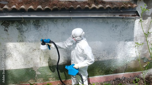 Quadro su tela Person in protective suit spraying disinfectant on a dirty wall outdoors, perfor